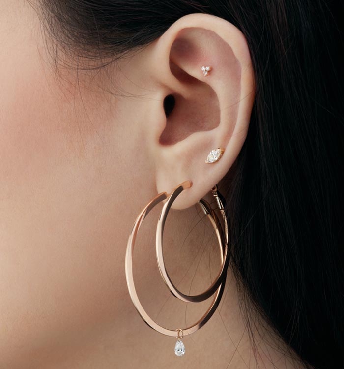 Gros plan sur une oreille avec une composition de boucles d'oreilles Maria Tash, des studs, des anneaux, des pendents agencés tout autour de l'oreille